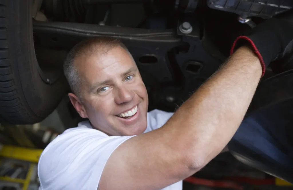 Smiling technician working under a car on a lift